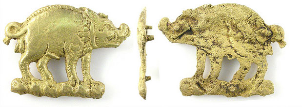 Three views of a brass-coloured badge in the shape of a boar, one the left a profile view looking right, in the middle a view looking straight ahead and on the right a view looking left. Along the left hand side and along the bottom are scale bars marked out in centimetres