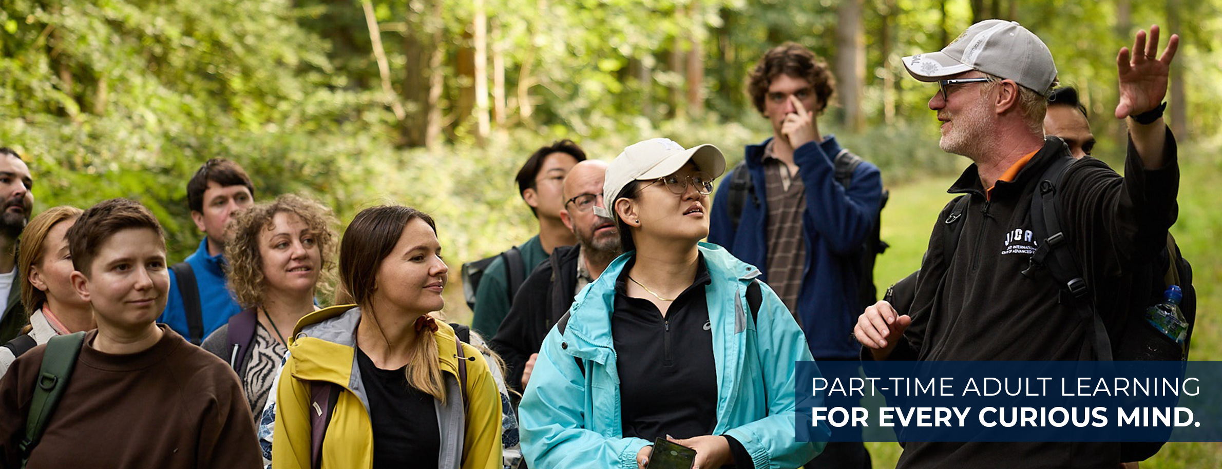 Students outside in a lush woodland listening to a tutor