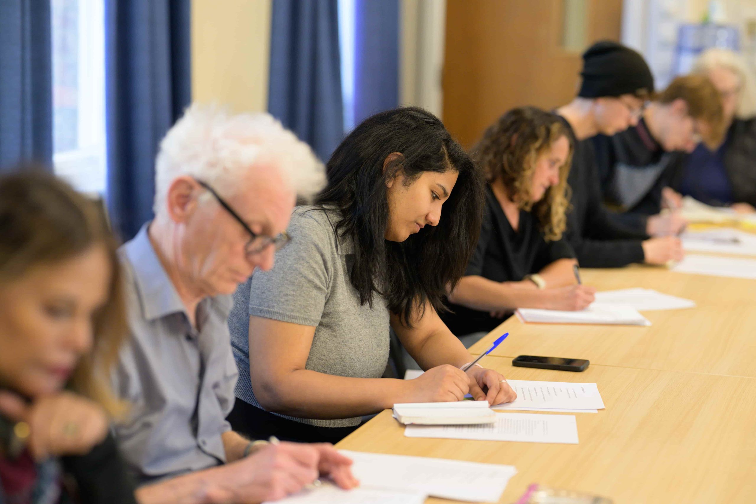 A group of students sit at a desk taking notes