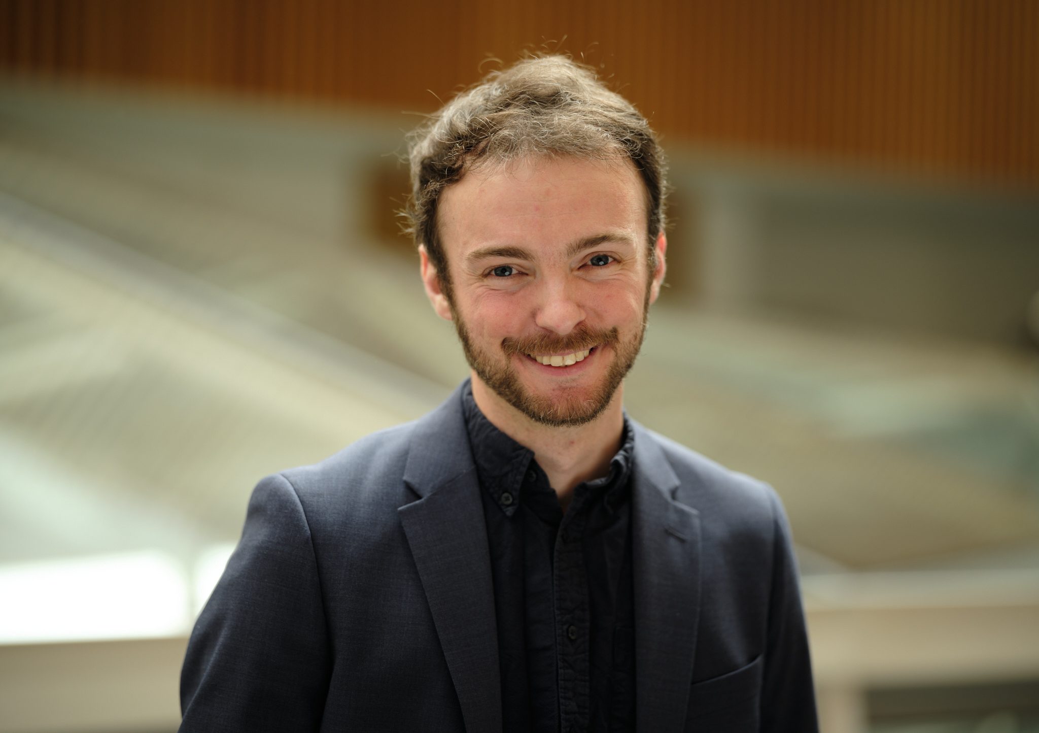Professional headshot of Samuel Recht, Director of Studies in Natural Sciences, wearing a dark suit, looking at the camera against a blurred background.