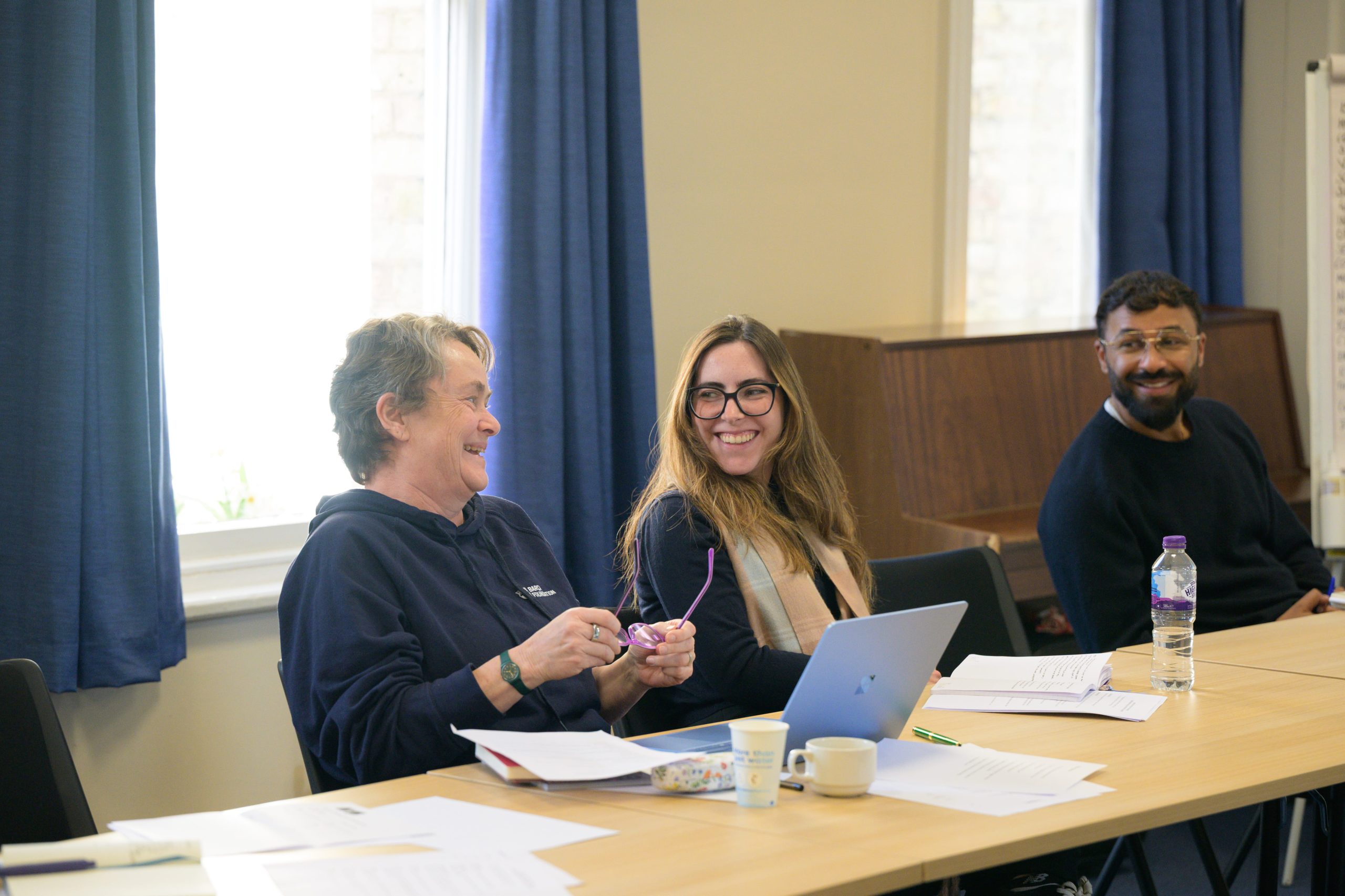 Students are sat together having a discussion. A woman moves her hands expressively to communicate her point.