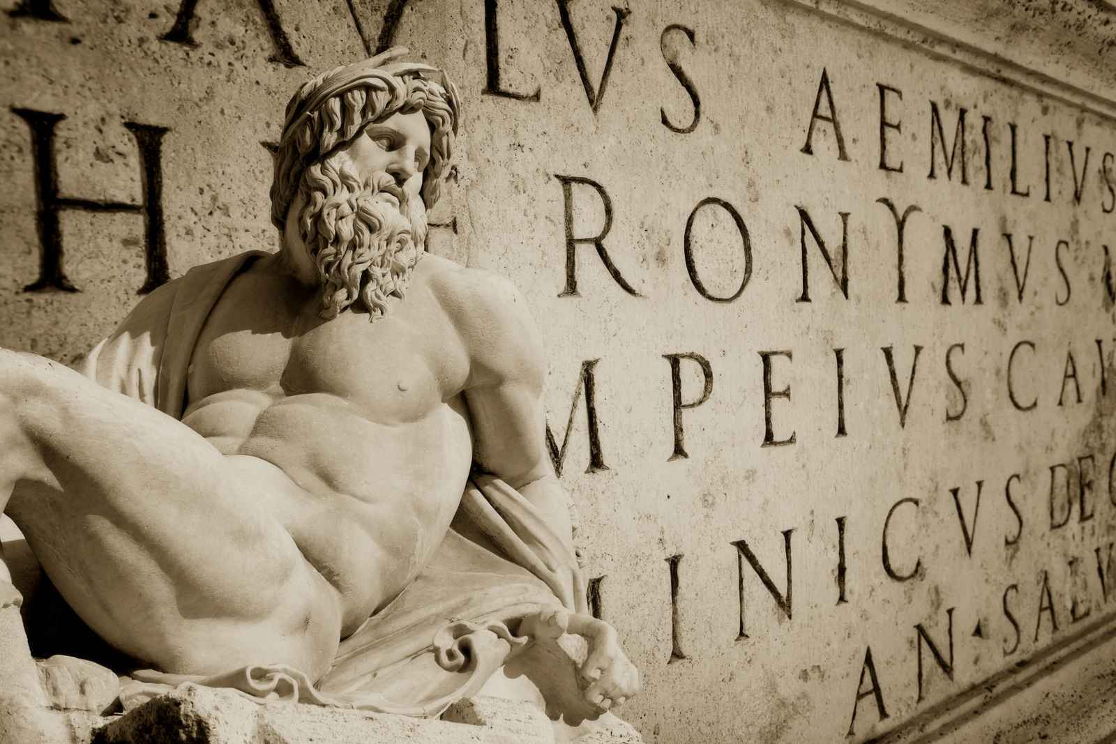 A Roman-style statue of a man in front of letters carved into stone.