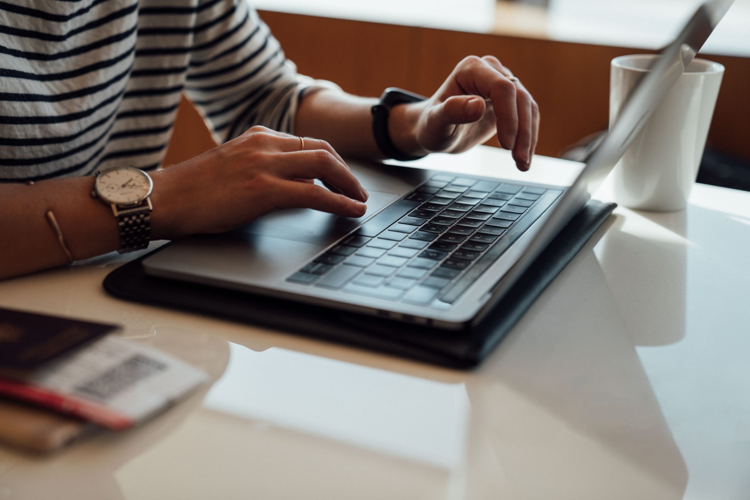 Photo of hands typing on laptop at desk surrounded by paper.