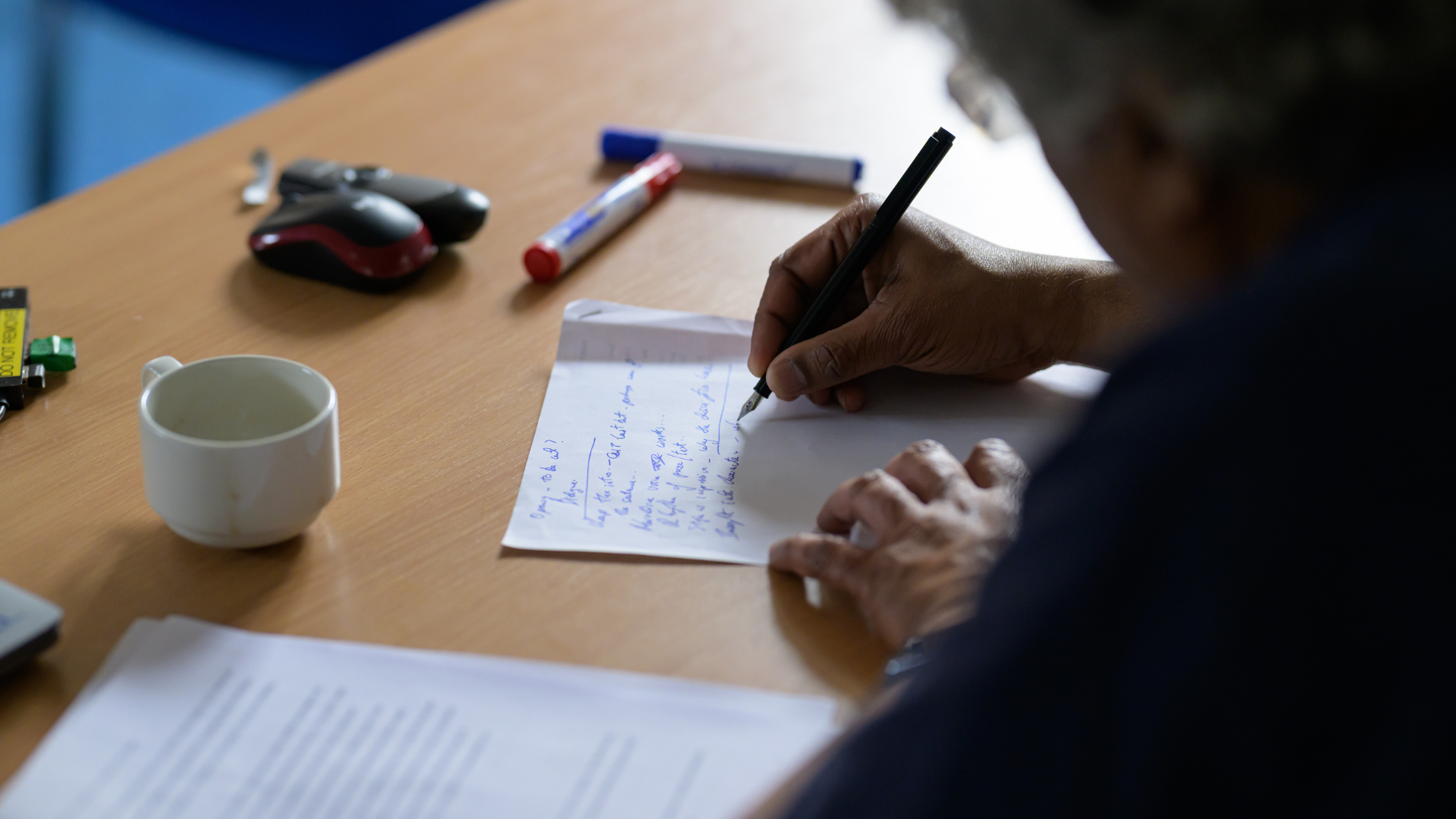 A close-up of a man's hands as he writes with ink pen while sat at a desk.