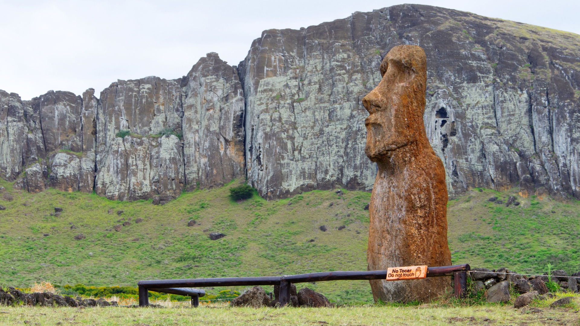 Moai statue on Easter Island against rocky cliffs and grassy plains, a historic Polynesian landmark.