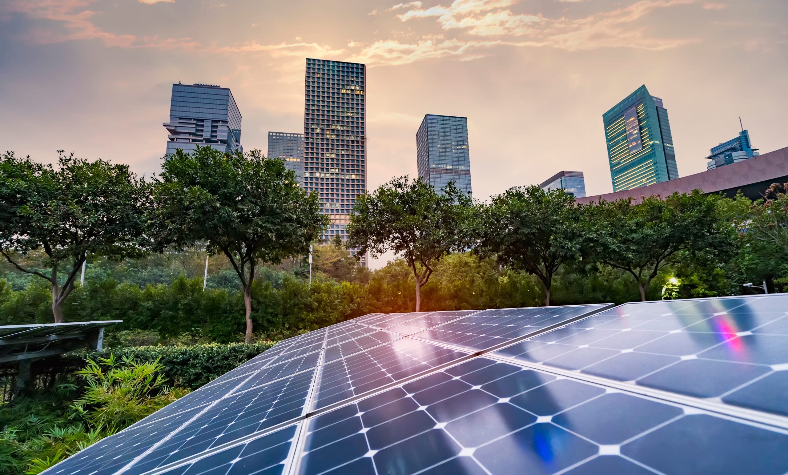 Sunset over city skyline, with prominent green spaces and solar panels.