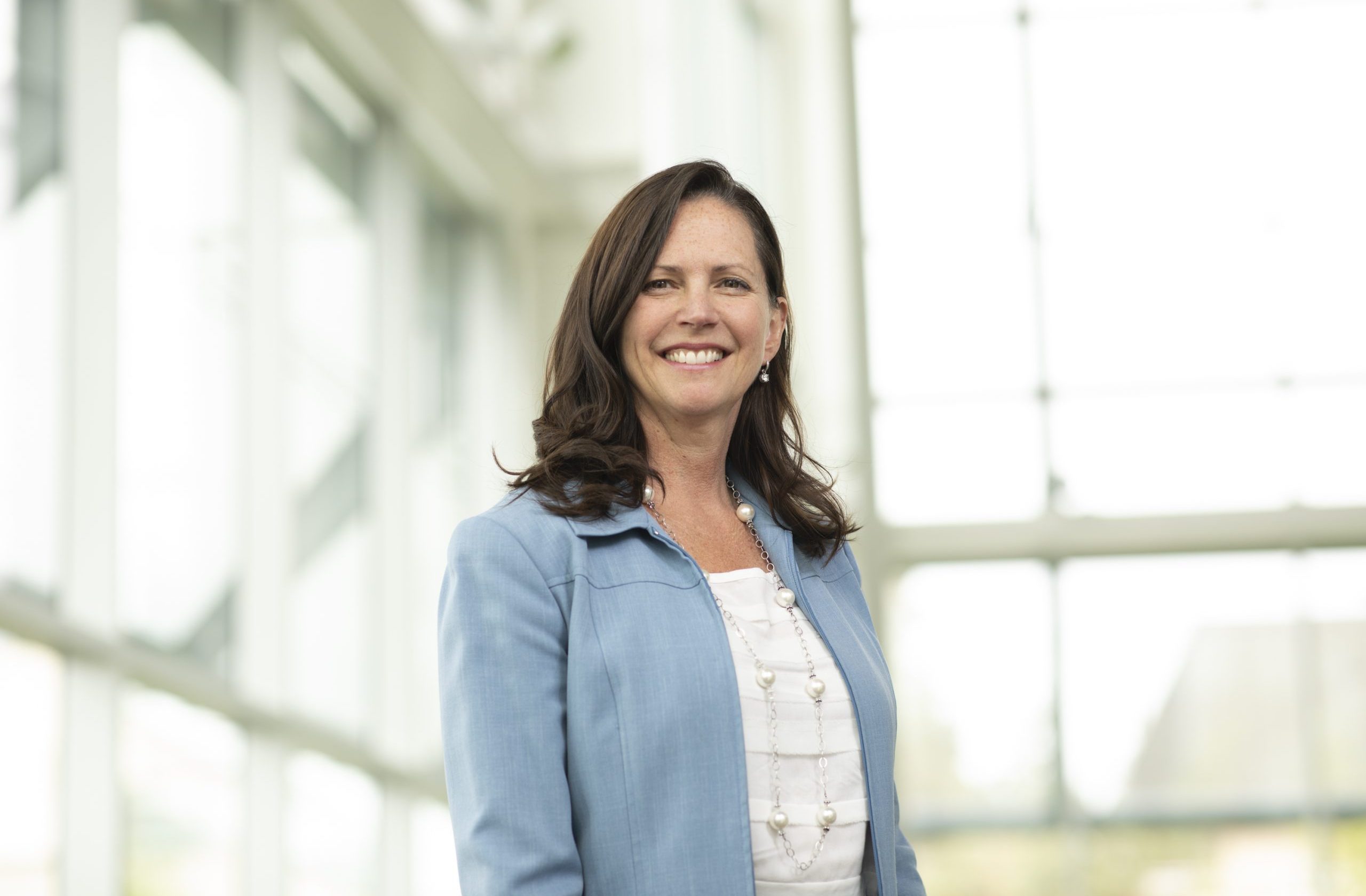 Professional headshot of Sheila LeBlanc, Visiting Fellow, wearing a blue blazer, looking at the camera against a light background with windows.