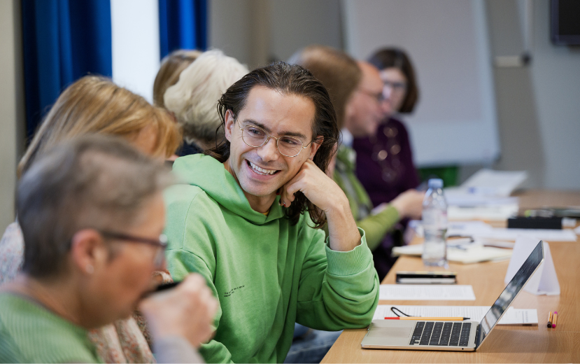 A history of art student in a classroom setting speaking to a classmate, smiling.