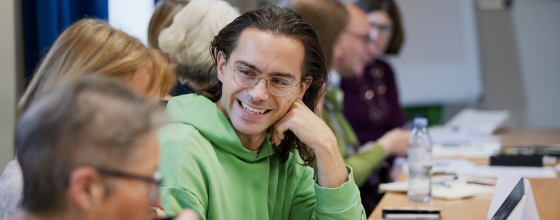 A history of art student in a classroom setting speaking to a classmate, smiling.